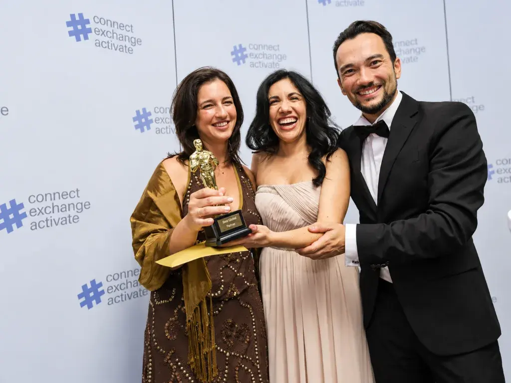 Three colleagues in evening wear laughing together as one holds a golden Best Global Partner statuette