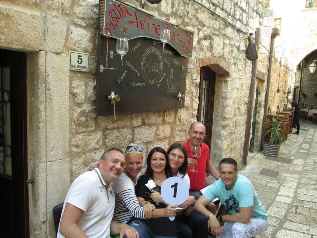 A team celebrating outside a stone wine bar with a number 1 team sign and glasses of red wine