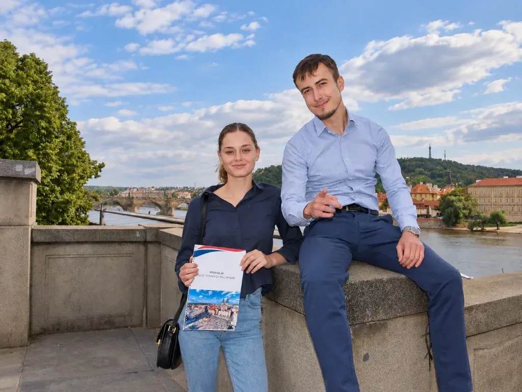 A couple of teammates posing on a stone wall by the river holding their challenge booklet