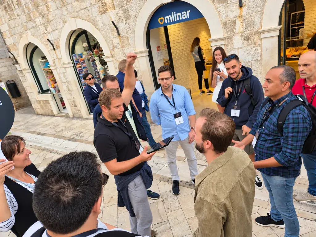 A team gathered in a stone-paved square, one member raising an arm while holding a tablet