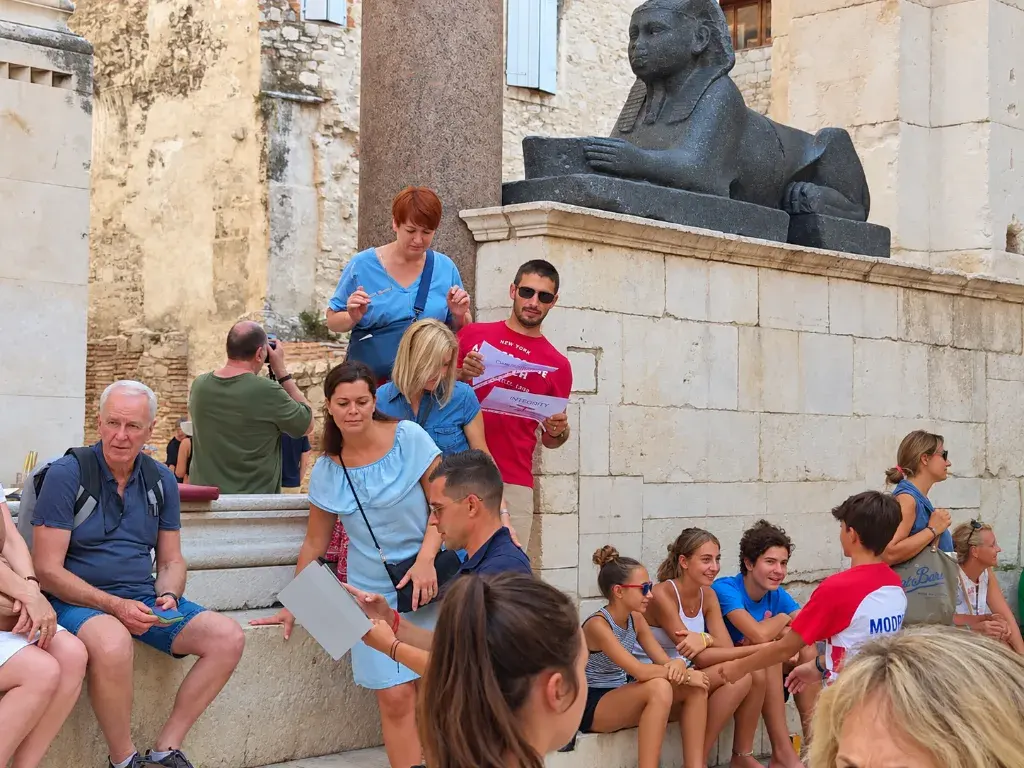 Teams gathered around a stone sphinx statue, reading their clue sheets in the Old Town